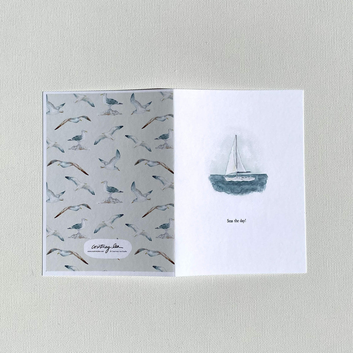 Greeting card with seagull pattern on one side and sailboat illustration on the other, on a textured surface.